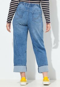 Pantalones vaqueros de mezclilla azul claro con cinturilla elástica, pierna recta y puños doblados. Cuentan con dos bolsillos traseros y un detalle de costura sutil.