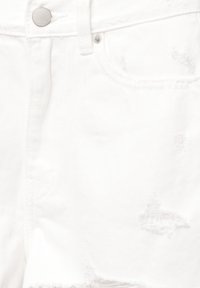Jean en denim blanc en gros plan montrant la poche avant, la passants de ceinture, le bouton en métal et les détails du tissu usé.