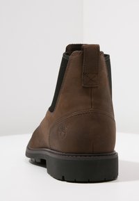 Brown leather ankle boot with elastic side panels, a pull tab, and a rubber sole. Features subtle logo on the outer side.