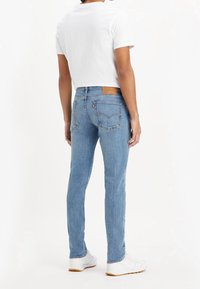 Ljusblå denimjeans med rak passform, utrustade med bakfickor, en brun läderlapp och vita sneakers. Materialet ser mjukt och texturerat ut.