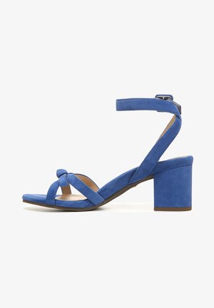 Suède blauwe haksandalen hebben een brede blokhak, een gevlochten knoopdetail en een verstelbare enkelriem voor een veilige pasvorm.