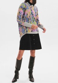 Flerfärgad tröja med ormskinnsmönster och grå muddar, ihop med en svart kordflorskjol med guldknappar och knähöga svarta stövlar.