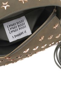 Borsa verde oliva con borchie a stella in oro rosa, chiusura con zip e una etichetta di tessuto all'interno con la scritta "DEVO RESISTERE... L'HO COMPRATA".