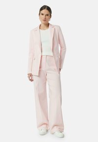 Completo rosa chiaro composto da un blazer e pantaloni a gamba larga, abbinato a un top rigato bianco e sneakers bianche. Tessuto di trama liscia.