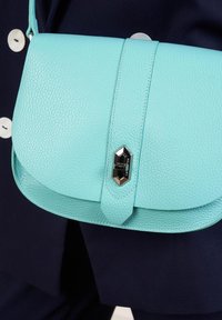 Borsa a tracolla in pelle texturizzata blu chiaro con chiusura magnetica e hardware argento, caratterizzata da un flap arrotondato e cinturino regolabile.