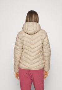 Beige pufferjakke med hætte, med et chevron-quiltet design. Glat tekstur og slim fit. Bæres med lilla bukser.