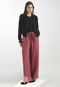 Zwarte bomberjack met een rits, gecombineerd met losse, met een trekkoord verstelbare wijde broek in stofroze, en zwarte flonkerige slides.