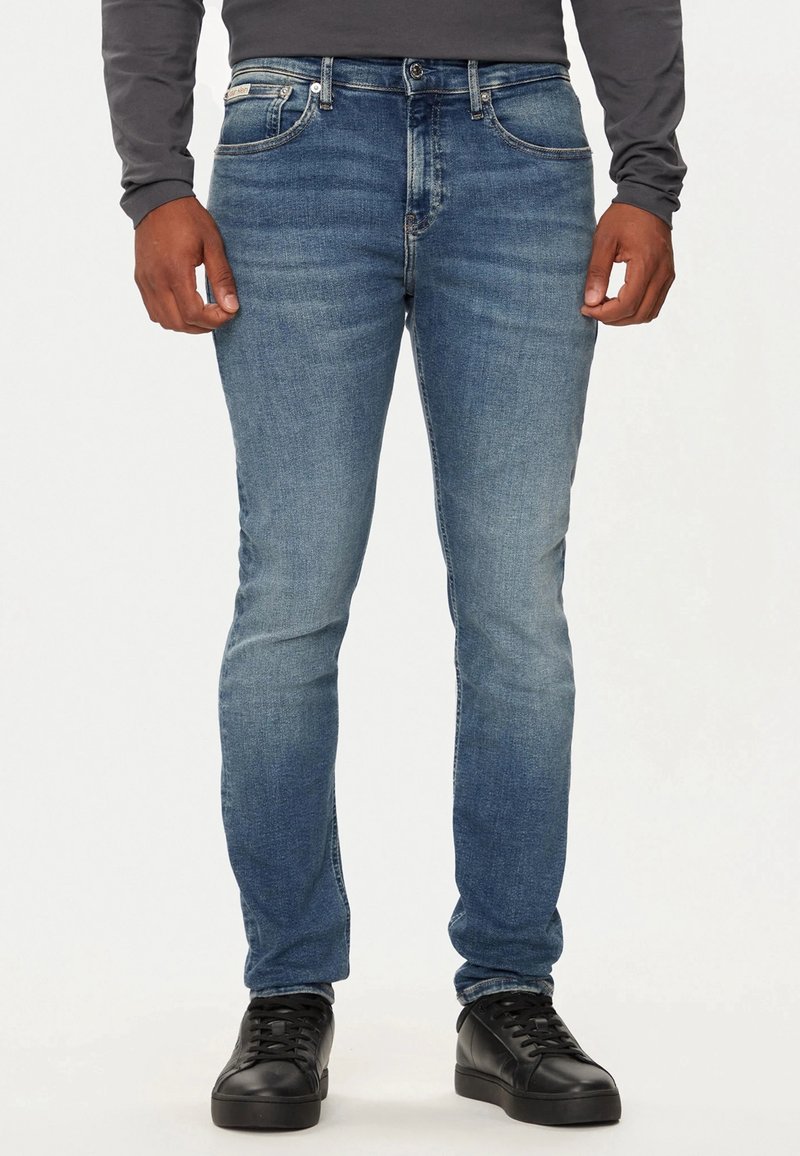 Jeans azules ajustados de denim, con un lavado desgastado, diseño de cinco bolsillos, costuras sutiles y una clásica cremallera de botones.