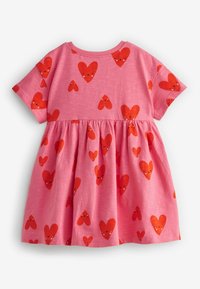 Robe en coton rose à manches courtes, présentant un motif de petits cœurs rouges. Taille froncée pour une silhouette de jupe évasée.