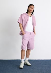 Light pink short-sleeve button-up shirt paired with matching knee-length shorts. Worn with a white T-shirt and greenish athletic shoes.