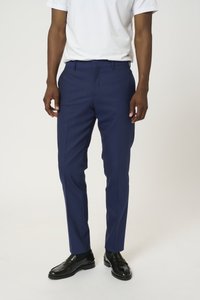 Pantalones de hombre en azul marino, diseñados con un corte entallado, fabricados con un tejido ligero, textura sutil y presillas para cinturón. Llevados con zapatos negros.