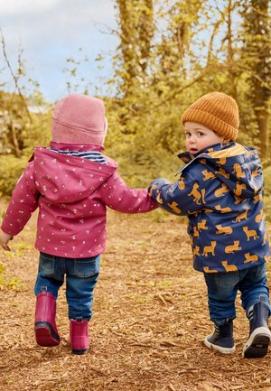 Divi bērni iet roku rokā, viens ar rozā ziedu lietusmēteli, bet otrs ar tumši zilu mēteli ar oranžiem dzīvnieku rakstiem, abi ar gumijas zābakiem.