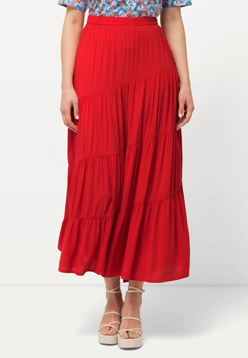Gonna maxi rossa con design a strati, tessuto leggero e waistband elastico. Abbinata a sandali con piattaforma beige.
