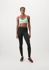 Jasnoniebieski stanik sportowy i czarne legginsy z wysokim stanem. Brązowe buty sportowe z kremową podeszwą. Prosty, dopasowany fason i elastyczny materiał.