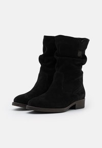 Bottines en suède noir avec un design décontracté, des détails cousus, un bout rond et un talon bas empilé. Présente une discrète étiquette de logo sur le côté.