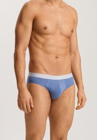 Slip da uomo in tessuto azzurro chiaro con una cintura elastica grigia sulla quale è stampato il nome del marchio "HANRO" in un testo chiaro. Texture liscia.