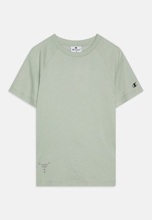 Világoszöld pamut póló rövid raglán ujjakkal, kerek nyakkal, és fekete logóval a bal ujján és az elülső alsó sarkán.