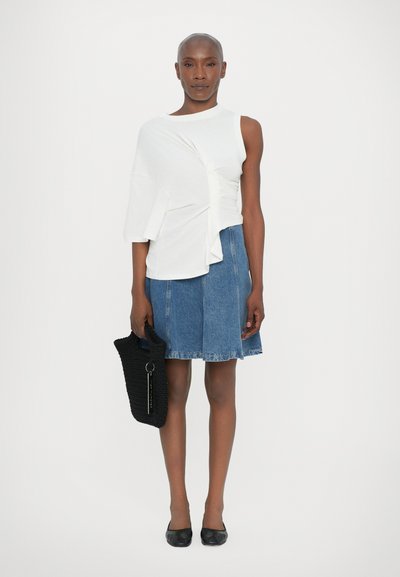Biely asymetrický top s detailom twist, skombinovaný s modrou denimovou A-liniovou sukňou. Čierna crochtovaná taška a čierne balerínky dopĺňajú vzhľad.