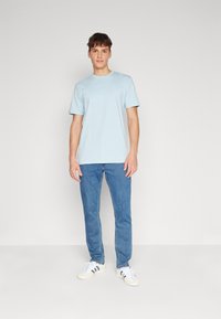 Camiseta de algodón de color azul claro con mangas cortas y un pequeño logo en el pecho, combinada con jeans de mezclilla azules y zapatillas blancas.
