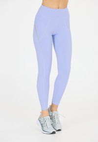 Ljust lila träningsleggings med hög midja, sidofickor och kontrasterande platta sömmar. Bärs med grå löparskor.