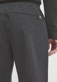 Mørkegrå joggebukser laget av teksturert stoff, med elastisk midjebånd og en liten merketagg på baksiden.