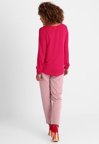 Ljusrosa långärmad blus med rund halsringning, matchad med ljusrosa byxor och röda högklackade skor. Strukturerad och slät finish.