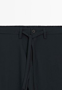 Pantalons noirs avec taille élastique, passants de ceinture, fermeture par bouton et une ceinture en tissu non nouée au centre à l'avant.