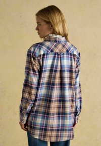 Plaid shirt in various shades of blue, brown, and cream. Features a button-down collar, cuffed sleeves, and a pleat detail at the back.