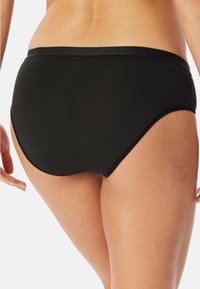Braguita negra de cintura alta con una textura suave, costuras laterales y una cinturilla elástica. El diseño presenta detalles minimalistas en la parte posterior.
