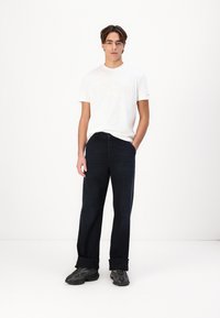 Lett hvit t-skjorte med preget tekst, sammen med mørkeblå denimjeans med avslappet passform og oppbrettede hem. Svart teksturerte sneakers.