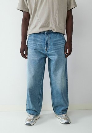 Hellblaue, oversized Jeans aus Denim mit einer verblassten Textur, straight-leg Design und subtilen Waschungen, kombiniert mit grauen Sneakers.