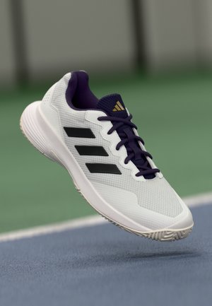 White athletic shoe with purple accents, black stripes, and mesh texture. Features a rubber sole with traction grooves.