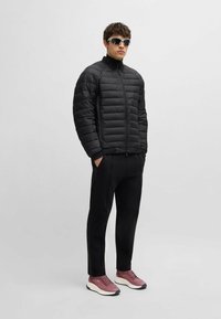 Svart pufferjacka med dragkedja fram och ribbade muddarna, tillsammans med svarta byxor och rosa träningsskor med vita sulor. Solglasögon ingår.