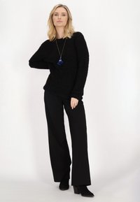 Schwarzer strukturierter Pullover, lockerer Schnitt, kombiniert mit schwarzen weit geschnittenen Hosen und Ankle Boots. Ergänzt durch eine Halskette mit blauen Quasten.