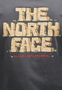 Το λογότυπο The North Face σχεδιασμένο ως πέτρινοι όγκοι με μικρά μπαλώματα χόρτου και το σύνθημα «Never Stop Exploring» (Μην σταματάς ποτέ να εξερευνάς) με κόκκινα γράμματα από κάτω.