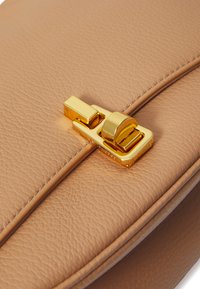 Borsa a mano beige in pelle con una texture liscia, dotata di una chiusura in metallo dorato, design piatto e dettagli di cucitura puliti.