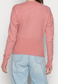 Pull en maille rose clair avec ourlet et poignets côtelés, doté d'une coupe décontractée et d'un col rond, associé à un pantalon en denim bleu clair.