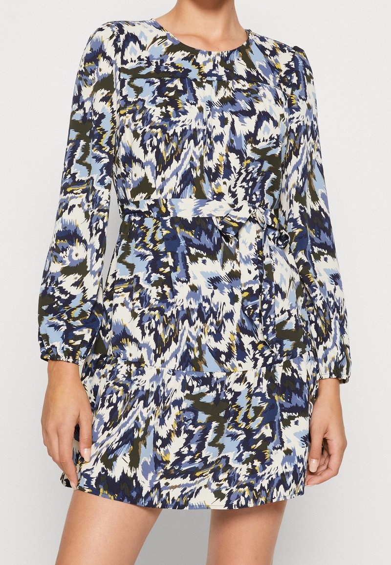 Mekko, jossa on pitkät hihat ja sininen, valkoinen ja vihreä abstrakti kuvio. Kestävä kangas, jossa on röyhelöhelma ja vyötärösidontayksityiskohta.