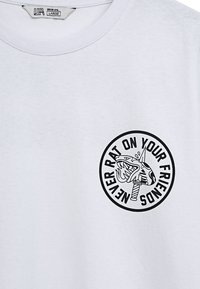 Biała bawełniana koszulka z okrągłym czarnym grafiką przedstawiającą rekina oraz napisem "NIGDY NIE ZDRADZAJ SWOICH PRZYJACIÓŁ" w odważnych literach.