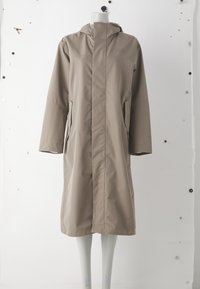 Beige vattentät jacka med huva, långa ärmar och framzippering. Har två sidofickor och en rak design som går till knäna.
