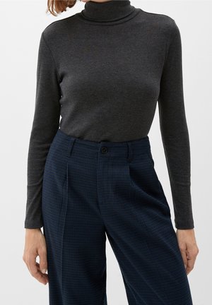 Woman wearing a fitted dark gray turtleneck sweater and high-waisted navy blue plaid trousers with a button closure.