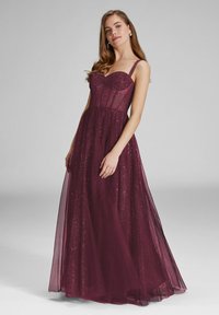 Robe longue bordeaux scintillante avec une superposition transparente, un corsage structuré, des bretelles ajustables et une silhouette fluide. Texture scintillante sur toute la surface.