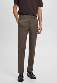 Brown tailored trousers with a flat front and belt loops, featuring side pockets and a slim fit, paired with black shoes.