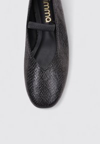 Zapato plano Mary Jane de cuero negro texturizado con tira elástica en la parte superior, visto desde arriba sobre un fondo claro.