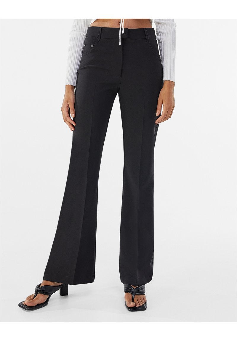 Svarta figurnära byxor med raka ben, som har sidofickor och silverfärgade detaljer. Slät väv med matt yta.