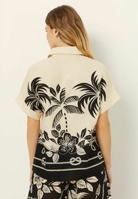 Korte mouwen overhemd gemaakt van lichte stof, met een crèmekleurige achtergrond en zwarte palmboom- en bloemenprints, en een geknoopte kraag.