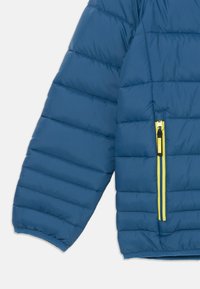 Μπλε τζάκετ πούφφας με μανίκι, με οριζόντια ραφή, περιλαμβάνει κίτρινη τσέπη με φερμουάρ και ελαστικούς καρπούς για ασφαλή εφαρμογή.
