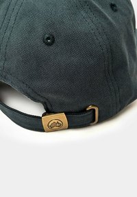 Gorra de béisbol gris oscuro con tejido texturizado, correa ajustable y herrajes de bronce que presentan un logo. Incluye ojales de ventilación.