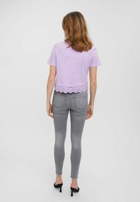 Fialové zkrácené tričko s vroubkovaným okrajem, spárované s těsnými šedými džíny a černými vysokými podpatky. Pohled ze zadu.