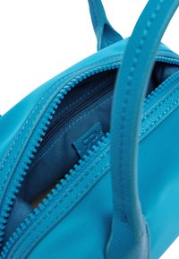 Mała niebieska torebka wykonana z teksturowanego materiału syntetycznego, z zamkiem błyskawicznym i wąskimi uchwytami. Wewnątrz znajduje się dopasowana niebieska podszewka.